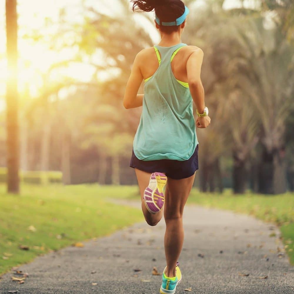 Woman in a visor, tank top, and shorts running alone on a park path