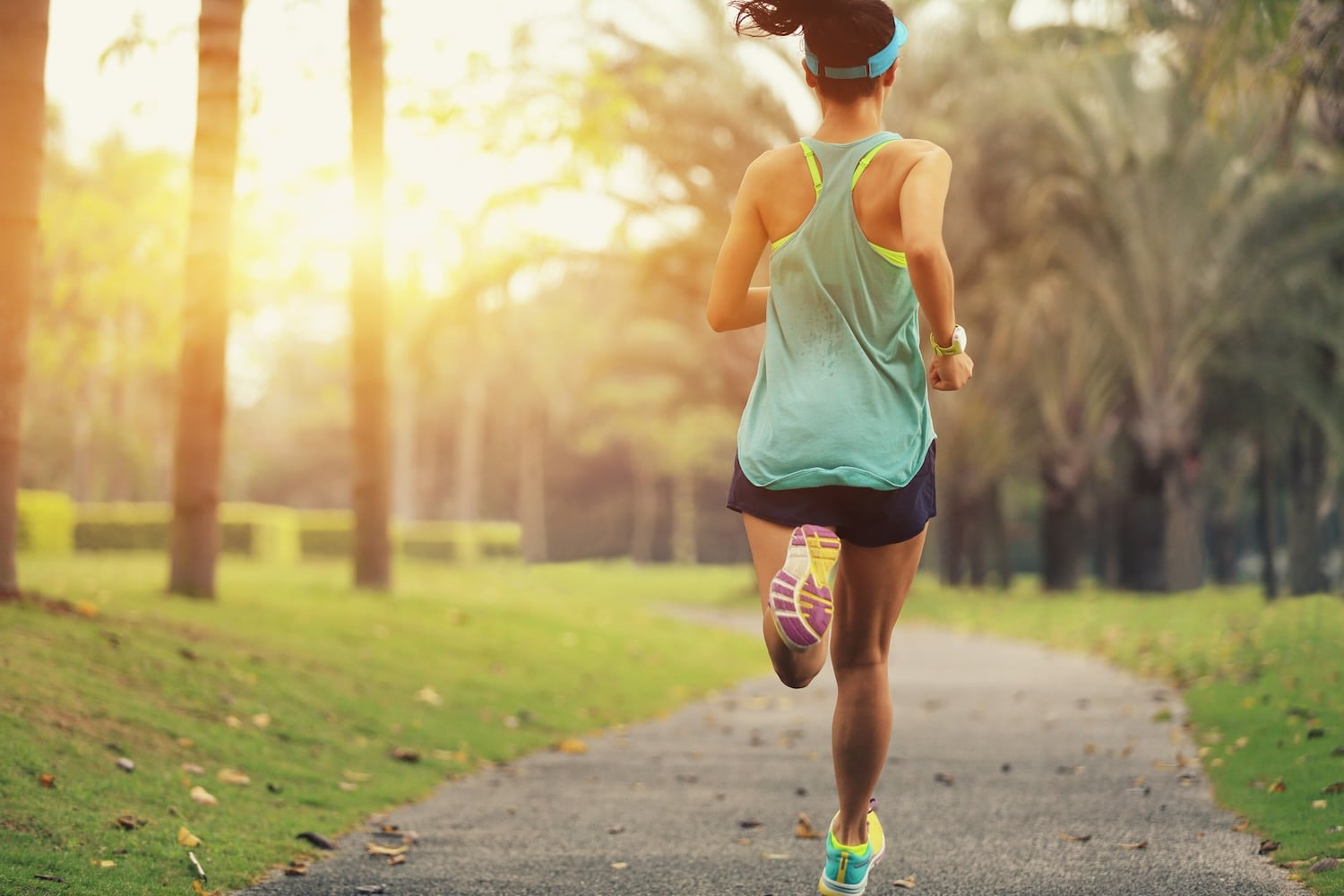 Woman in a visor, tank top, and shorts running alone on a park path