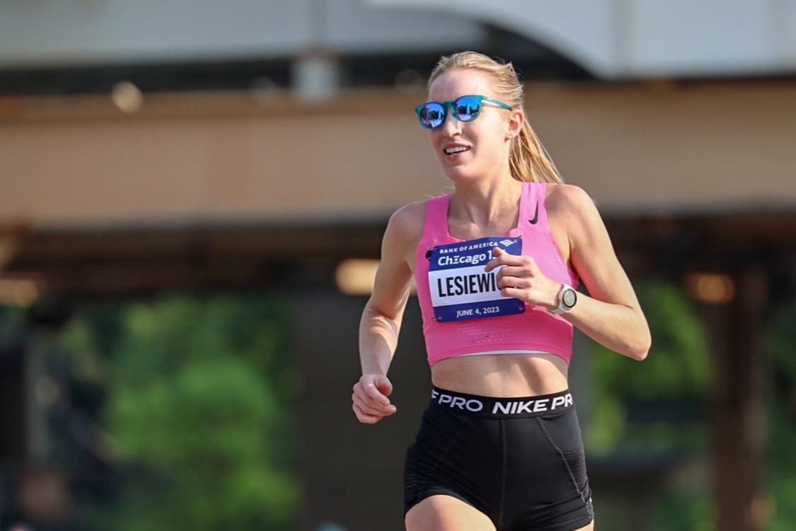 Image of Karen Lesiewicz in sunglasses, a pink top, and black shorts running a race with a blurred background